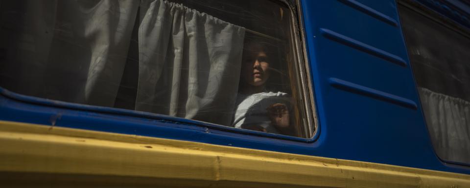 Une jeune fille déplacée regarde à travers la fenêtre d'un train en direct de l'Est de l'Ukraine. Le problème des enfants déplacés est particulièrement aigu, en particuliers lorsqu'il s'agit d'enfants ukrainiens déplacés de force en Russie qui ont été victimes de kidnapping et parfois de transfert forcé pour les "assimiler" à la tentative d'annexion de l'Ukraine par la Russie, sans que ces enfants soient de réels orphelins (image d'illustration). [Keystone/AP Photo - Nariman El-Mofty]