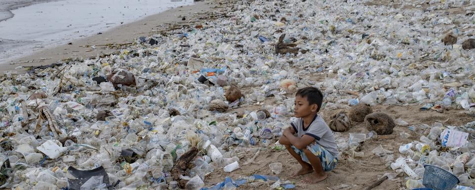 Un enfant assis sur une plage couverte de déchets plastiques à Kuta Beach à Bali, Indonésie, 31 décembre 2020. [EPA/Keystone - Made Nagi]