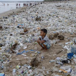 Un enfant assis sur une plage couverte de déchets plastiques à Kuta Beach à Bali, Indonésie, 31 décembre 2020. [EPA/Keystone - Made Nagi]