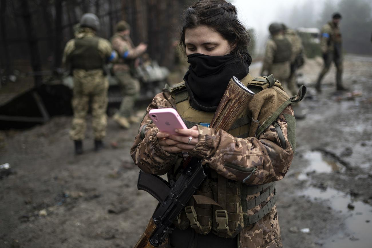 Une jeune soldate ukrainienne consulte son téléphone portable dans un village en périphérie de Kiev, le 1er avril 2022. [AP/Keystone - Rodrigo Abd]