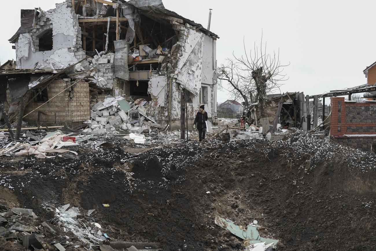 Une femme se tient au sommet d'un cratère près d'une maison détruite après une attaque à la roquette russe à Hlevakha, dans la région de Kiev, en Ukraine, jeudi 26 janvier 2023. [KEYSTONE - Roman Hrytsyna / AP Photo]
