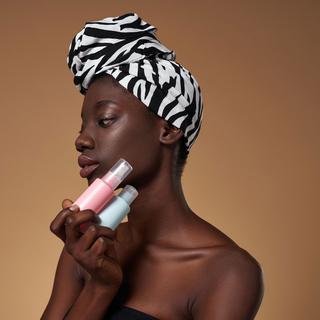 Une femme à la peau noire tient des produits cosmétiques devant son visage. [Depositphotos - LanaStock]