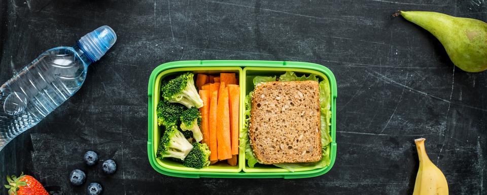 Un tupperware contenant du pain et des légumes entouré d'eau, d'amandes et de fruits. [Depositphotos - Pinkyone]