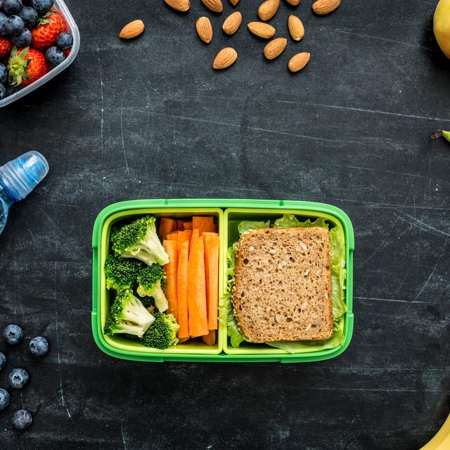 Un tupperware contenant du pain et des légumes entouré d'eau, d'amandes et de fruits. [Depositphotos - Pinkyone]