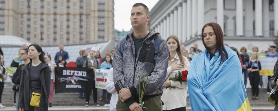 Des Ukrainiennes et ukrainiens observent une minute de silence en commémoration des soldats tués dans le conflit avec la Russie. [Keystone - EPA/Sergey Dolzhenko]