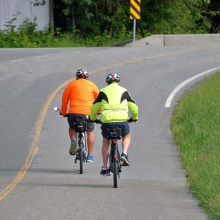 Deux cyclistes vêtus de vestes aux couleurs vives sur une route. [Depositphotos - modfos]