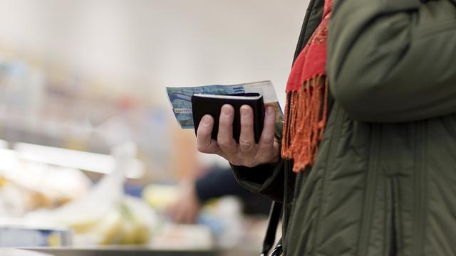 Une personne à la caisse d'un magasin tenant dans sa main son portemonnaie et un billet de 100 francs. [Keystone - Gaëtan Bally]