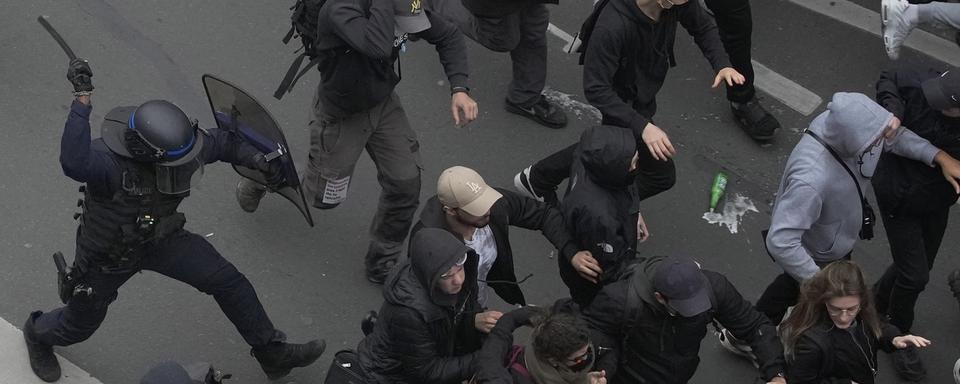 Un policier anti-émeute chasse des manifestants à l'aide d'une matraque à Paris, le 23 mars 2023. [Keystone - AP Photo/Christophe Ena]