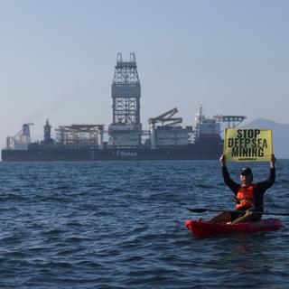 Un militant de Greenpeace brandit une pancarte face au navire d'exploitation minière en eaux profondes Hidden Gem, affrété par l'entreprise canadienne The Metals Company, alors qu'il rentre au port après huit semaines d'exploitation minière expérimentale dans le Pacifique au large du Mexique, le 16 novembre 2022. [Reuters - Gustavo Graf]