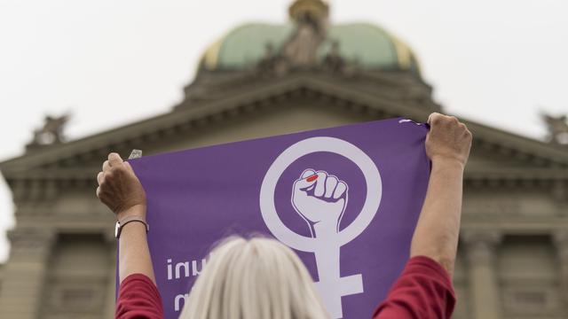 Une femme brandit le drapeau de la grève des femmes devant le Palais fédéral, le vendredi 14 juin 2019 à Berne. [Keystone - Alessandro della Valle]
