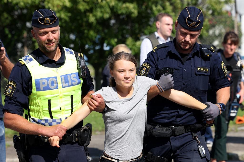 La militante pour le climat Greta Thunberg est emmenée par des policiers suédois après avoir participé à une nouvelle action pour le climat à Oljehamnen, à Malmö, peu après sa condamnation à une amende pour refus d'obtempérer lors d'une action de blocage en juin dernier dans la même ville. [AFP - Andreas Hillergren / TT News Agency]