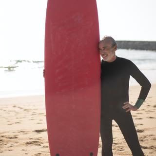 Un surfeur souriant au bord d'une plage. [Pexels - KampusProduction]