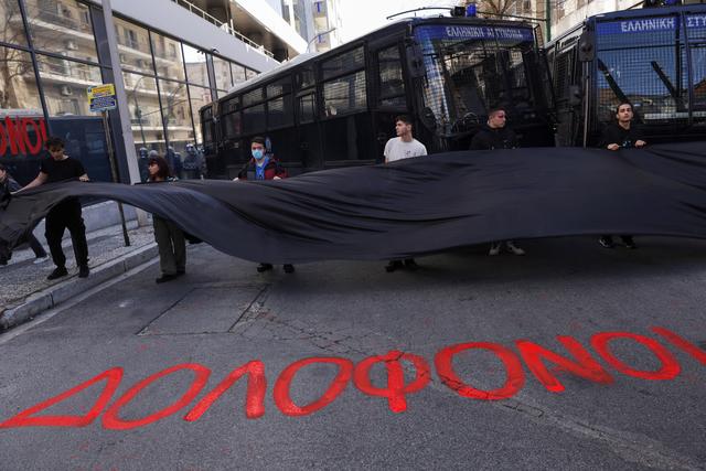 Des manifestants brandissent un drapeau noir devant des véhicules de police, derrière le slogan "Meurtriers" peint sur le sol. [reuters - Louiza Vradi]