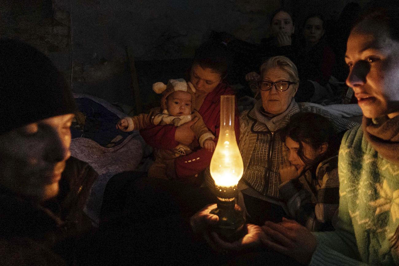 Personnes assises autour d'une lampe dans un abri anti-aérien à Marioupol, le dimanche 6 mars 2022. [Keystone - AP Photo/Evgeniy Maloletka]