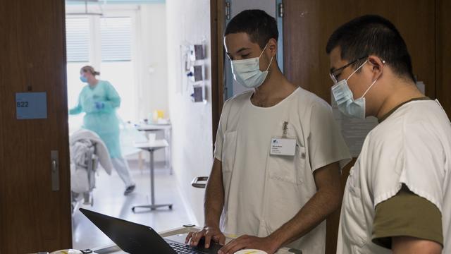 Les soldats Liu Kelun, à droite, et Andreas von Bueren saisissent les données d'un patient Covid-19 que leur transmet l'infirmière, à l'hôpital fribourgeois (HFR), le mercredi 8 avril 2020 à Fribourg. [Keystone - Alessandro della Valle]