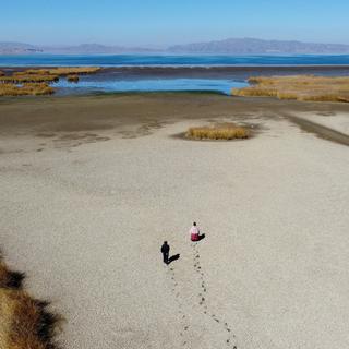 Deux personnes marchent sur le lit asséché et craquelé près de la rive du lac Titicaca pendant la saison de la sécheresse à Huarina, en Bolivie, le 3 août 2023. [Reuters - Claudia Morales]