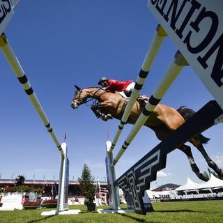 Le cavalier olympique suisse Steve Guerdat et le cheval de compétition Bianca entre deux obstacles sponsorisés par une marque horlogère helvétique haut de gamme. [Keystone - Gian Ehrenzeller]