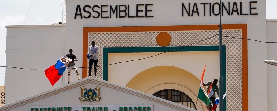 Des manifestants arborant des drapeaux du Niger et de la Russie escaladent la porte de l'Assemblée nationale en soutien au coup d'État militaire au Niger (image d'illustration). [Keystone/EPA - Issifou Djibo]