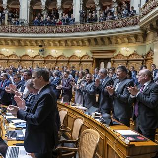 Les membres du Parlement suisse s'applaudissent après la réélection du Conseil fédéral. [Keystone - Peter Schneider]