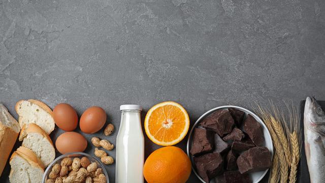 Des aliments potentiellement allergènes sont posés sur une table: du pain, des oeufs, des cacahuètes, du lait, des oranges, du chocolat, du blé et du poisson. [Depositphotos - NewAfrica]