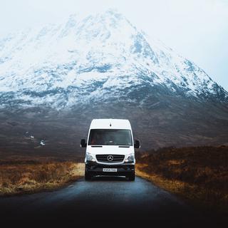 Un van roule sur une route dans les montagnes. [Unsplash - Jordan Irving]