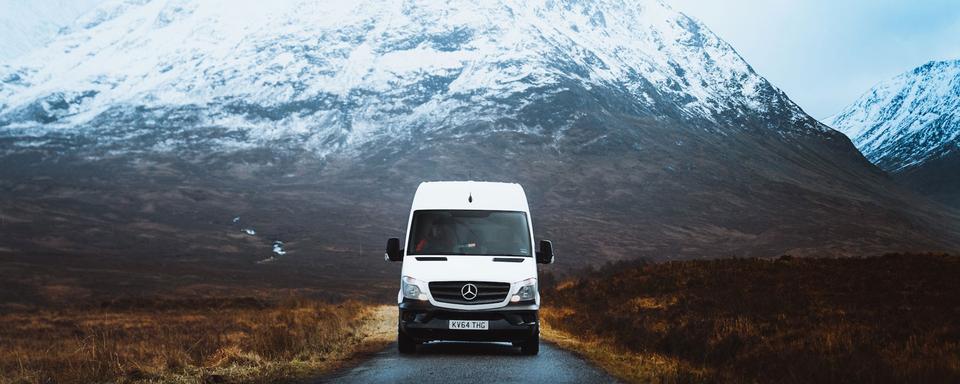 Un van roule sur une route dans les montagnes. [Unsplash - Jordan Irving]