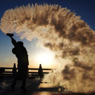 Un touriste verse verse de l'eau en l'air au lever du soleil à Fuyuan, dans la province de Heilongjiang, en Chine, le 14 janvier 2023. [EPA/ Keystone - Xinhua/Wang Jianwei]