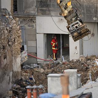 Un pompier regarde une excavatrice qui déplace des déblais sur le site d'une explosion à Marseille. [AFP - Nicolas Tucat]