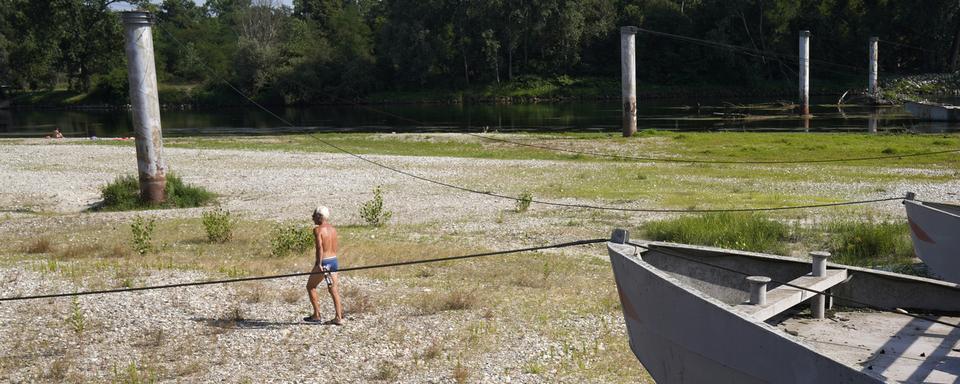 Un homme se ballade dans le fond asséché de la rivière Ticino vers Milan (Italie, 2023). [Keystone/AP Photo - Antonio Calanni]