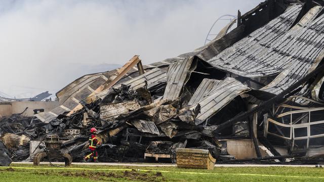 Un pompier marche autour des décombres après l'incendie d'une ferme à Bottens. [Keystone - Jean-Christophe Bott]