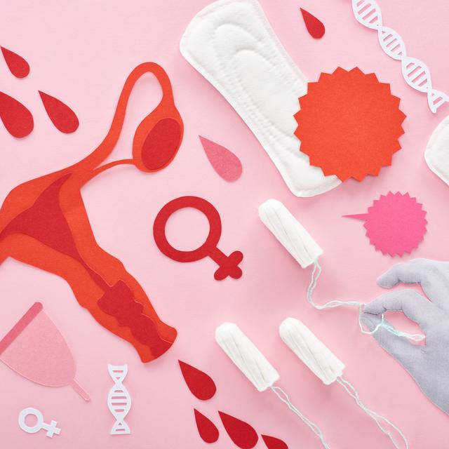 Sur fond rose, des ovaires sont représentés entourés d'une coupe menstruelle, de tampons et de serviettes hygiéniques. Une main tient les cordes d'un tampon. [Depositphotos - VadimVasenin]