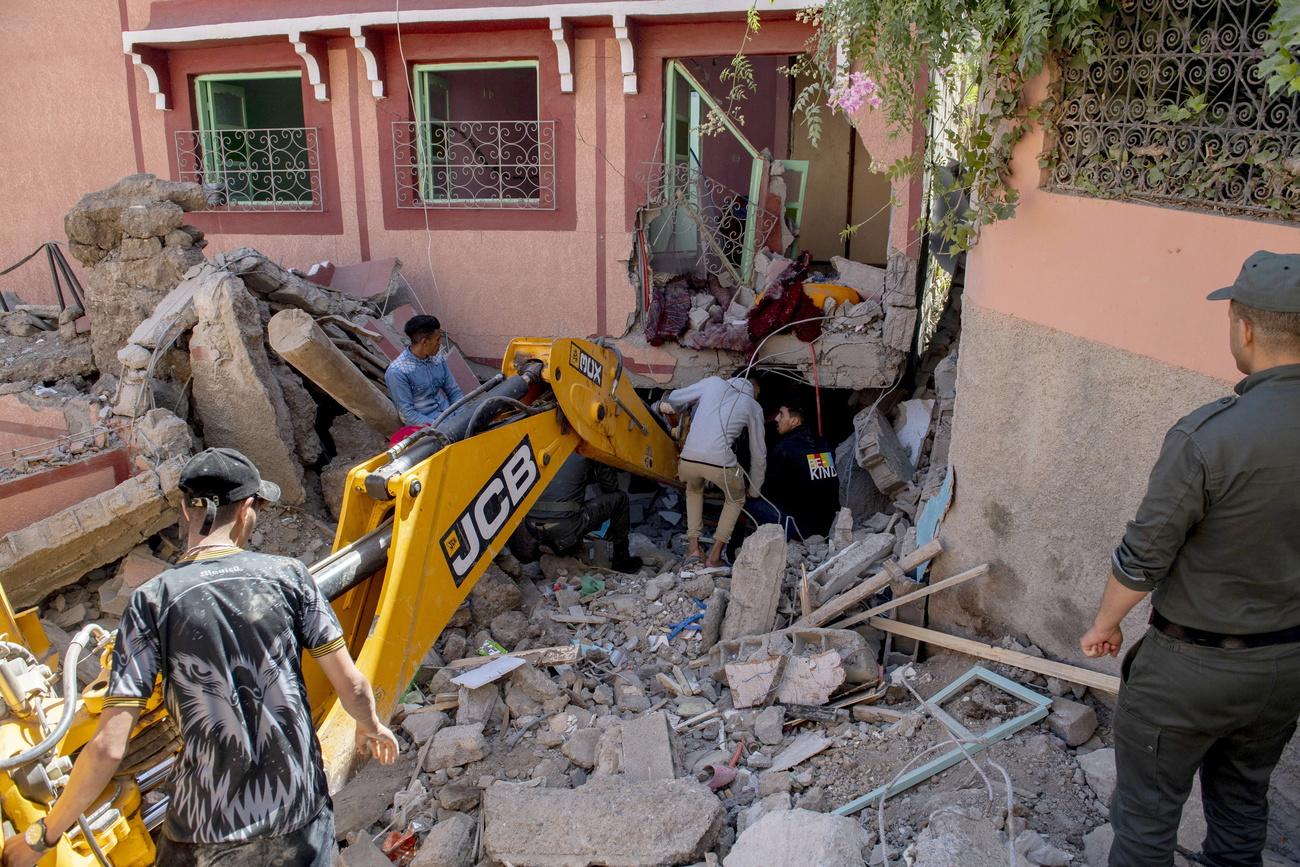 Des personnes fouillent les décombres d'un bâtiment endommagé à l'aide d'une pelleteuse à la suite d'un tremblement de terre à Marrakech, au Maroc, le 9 septembre 2023. [Keystone - JALAL MORCHIDI]