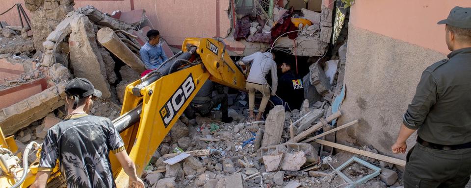 Des personnes fouillent les décombres d'un bâtiment endommagé à l'aide d'une pelleteuse à la suite d'un tremblement de terre à Marrakech, au Maroc, le 9 septembre 2023. [Keystone - JALAL MORCHIDI]