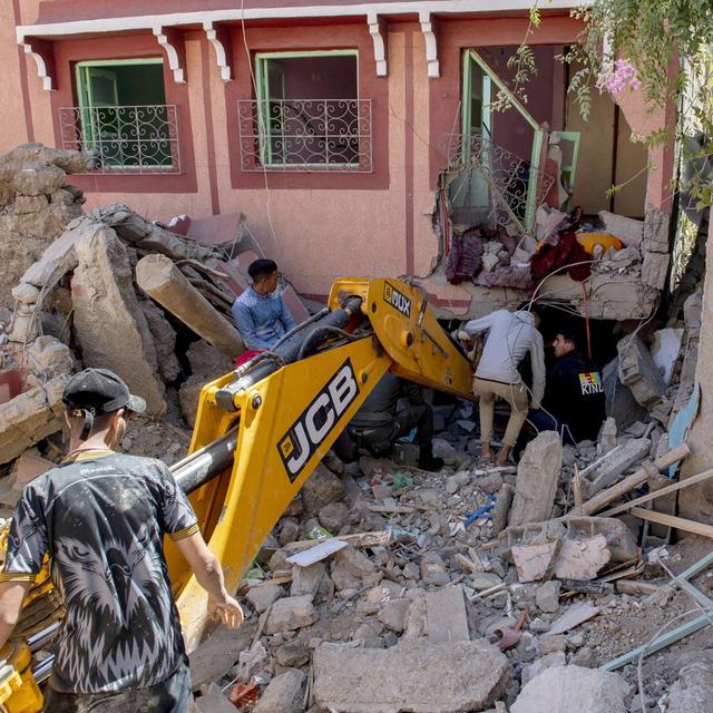 Des personnes fouillent les décombres d'un bâtiment endommagé à l'aide d'une pelleteuse à la suite d'un tremblement de terre à Marrakech, au Maroc, le 9 septembre 2023. [Keystone - JALAL MORCHIDI]