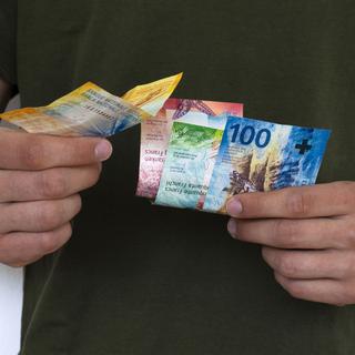 Gros plan sur deux mains qui tiennent des billets de francs suisses. [Depositphotos - p.sgarbosky.gmail.com]
