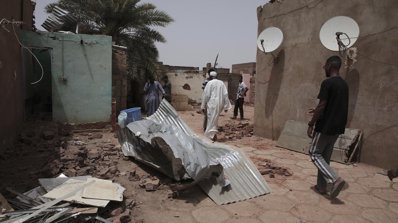 Des personnes marchent devant une maison touchée lors des récents combats à Khartoum, au Soudan, le mardi 25 avril 2023. [Keystone]
