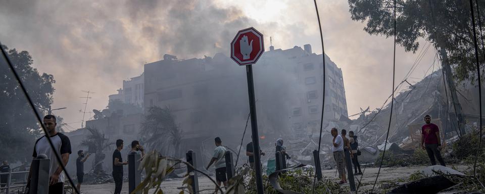 Des Palestiniennes et Palestiniens inspectent les débris d'un immeuble après une attaque de roquettes israéliennes, le 8 octobre 2023. [Keystone/AP Photo - Fatima Shbair]