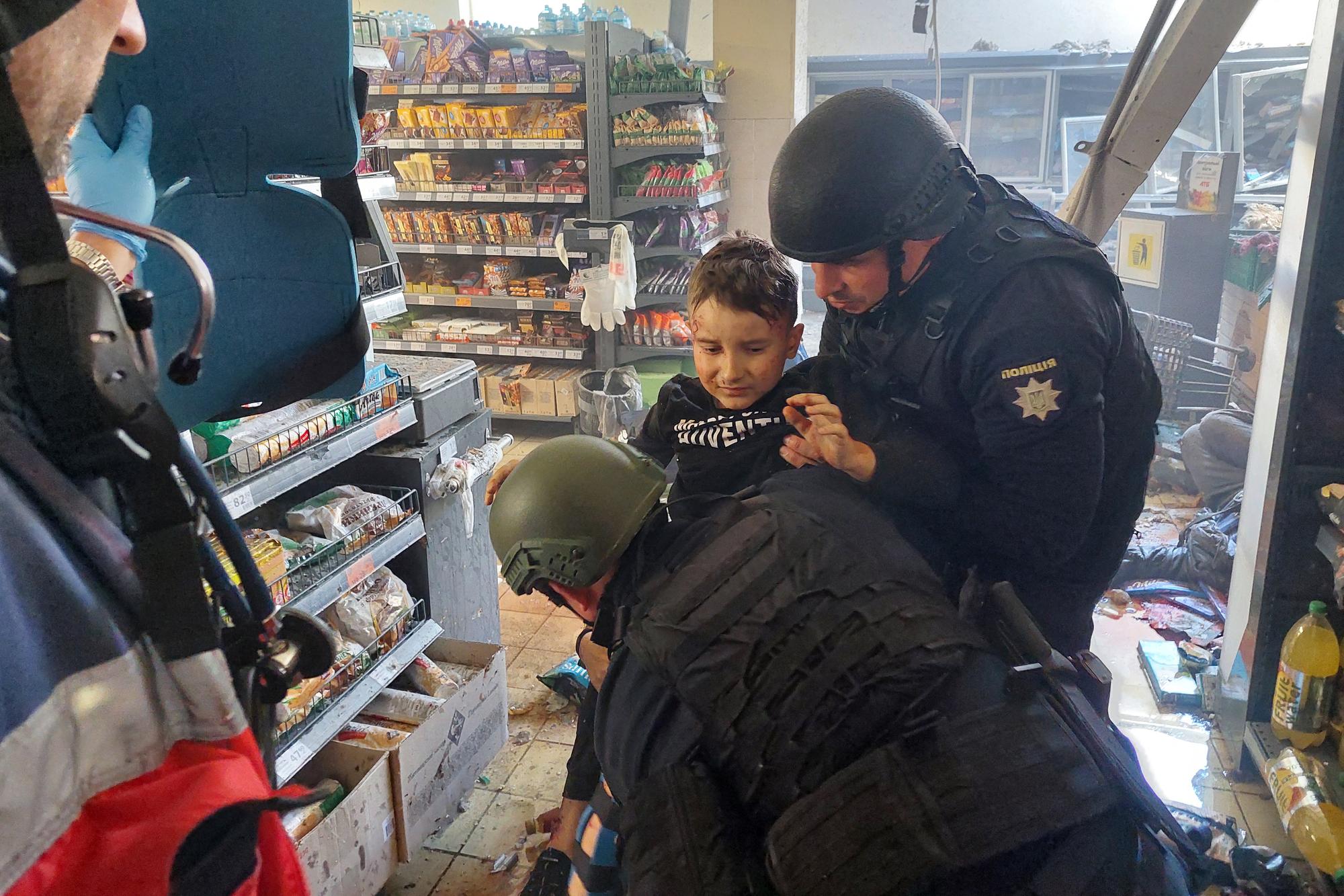 Un enfant blessé aidé par des policiers dans un supermarché à Kherson, le 3 mai 2023. [AFP - DINA PLETENCHUK]