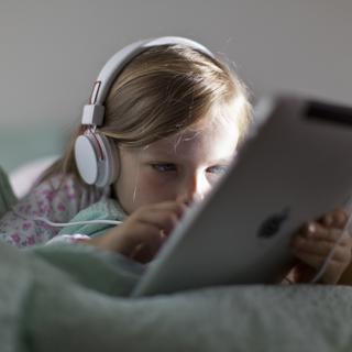Une enfant de sept ans écoute de la musique et regarde un Ipad. [Keystone - GAETAN BALLY]