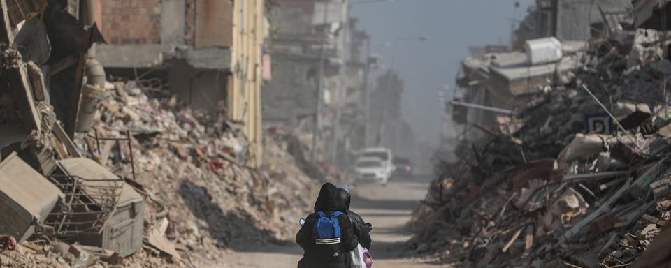 Des personnes passent sur une motocyclette devant des bâtiments effondrés à la suite de puissants tremblements de terre à Hatay, en Turquie. [Keystone - EPA/ERDEM SAHIN]