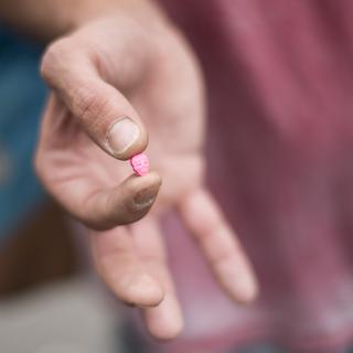 Un homme montre une pilule de MDMA, une drogue de la catégorie des amphétamines, connue pour ses effets stimulants et hallucinants (image d'illustration). [Keystone - Ennio Leanza]