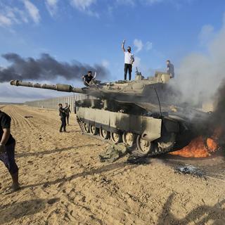 Des Palestiniens célèbrent la destruction d'un char israélien à la barrière de la bande de Gaza, à l'est de Khan Younis, dans le sud du pays, le samedi 7 octobre 2023. [Keystone - Hassan Eslaiah]