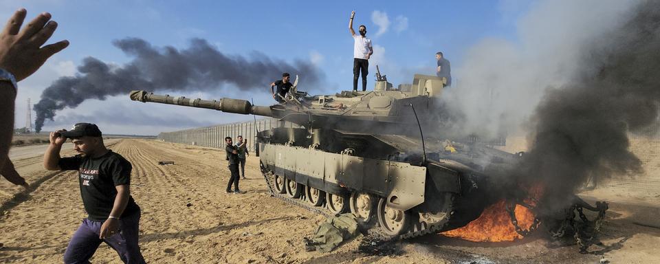 Des Palestiniens célèbrent la destruction d'un char israélien à la barrière de la bande de Gaza, à l'est de Khan Younis, dans le sud du pays, le samedi 7 octobre 2023. [Keystone - Hassan Eslaiah]