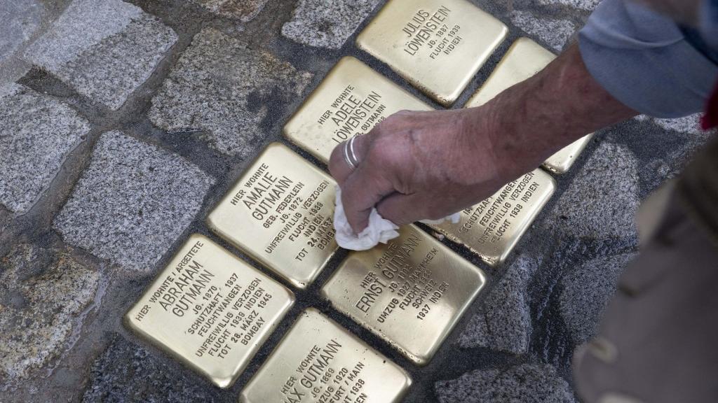 Gunter Demnig, fondateur du projet Stolpersteine (littéralement, "pierres sur lesquelles on trébuche"), nettoie celles qu'il vient de placer au sol, en commémoration de la famille Gutmann, à Feuchtwangen. Ces personnes ont eu la vie sauve grâce à leur fuite en Inde en 1939. Bavière, le 30 mai 2023. [AFP - Thomas Kienzle]