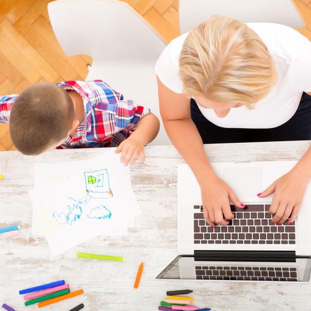 Une mère travaille sur son ordinateur à côté de son fils qui dessine. [Depositphotos - Spectral]