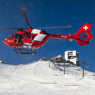 Un hélicoptère de la Rega survole une zone lors d'un exercice avalanche organisé par la Rega et le Secours alpin romand (SARO) sur le Glacier 3000, vendredi 6 décembre 2019, aux Diablerets. [KEYSTONE - Jean-Christophe Bott]