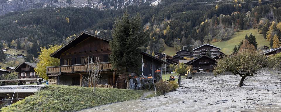 Des membres de la Protection civile nettoient une lave torrentielle au milieu du village de Champery. [Keystone - Noemi Cinelli]