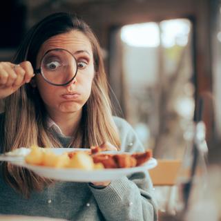 Dans un restaurant, une femme examine son assiette avec une loupe. [Depositphotos - Nicoletaionescu]