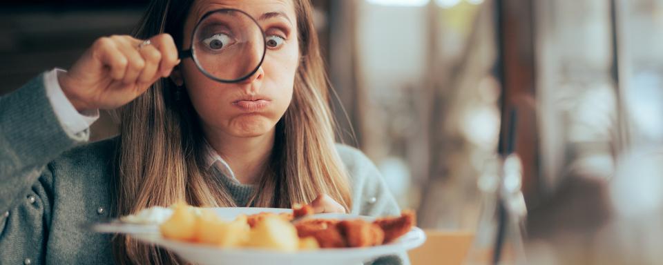 Dans un restaurant, une femme examine son assiette avec une loupe. [Depositphotos - Nicoletaionescu]