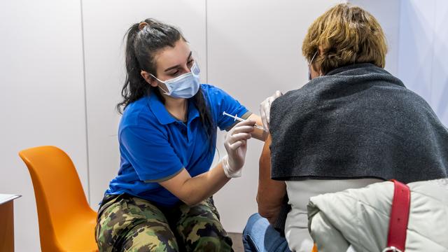 Une militaire vaccine une personne avec le vaccin moderna dans le centre de vaccination de Polyexpo le mardi 21 décembre 2021 à La Chaux-de-Fonds. [Keystone - Jean-Christophe Bott]
